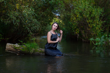mystical woman in black dress splashes in the river