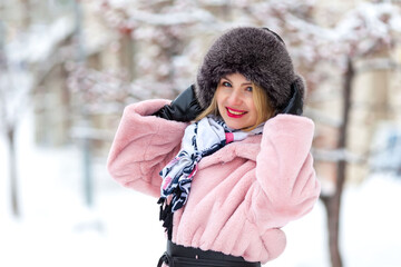 happy woman in a pink faux fur coat in winter on a background of snowy trees