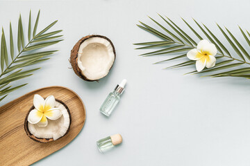 Fototapeta na wymiar Coconut essential oil and palm leaf oil on a table with copy space on a pastel background. Styled composition of flat lay with tropical leaves and flowers.