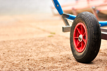 Closeup of red, black and blue boat launching dolly trailer rubber wheels on a slipway with red...