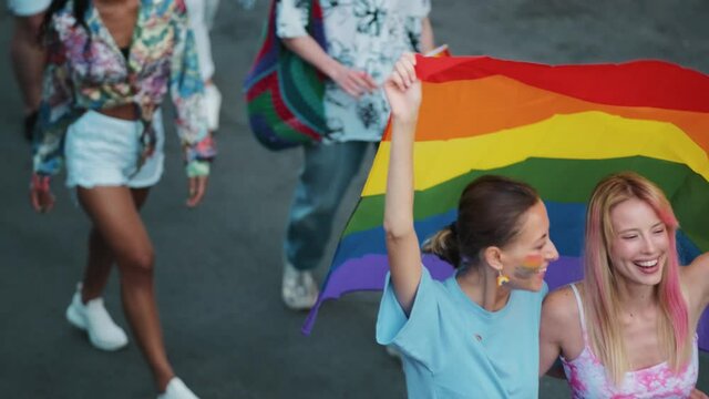 A group of lgbt people are walking on the street holding and waving colorful flag during pride gay parade