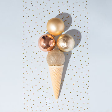 Christmas decoration gold baubles in ice cream cone. New Year minimal concept. Pastel blue background with glitter.