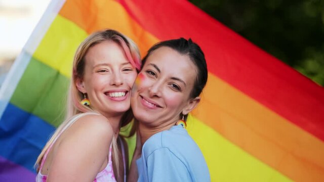 A smiling lesbian girls with rainbow make-up are kissing each other during pride gay parade