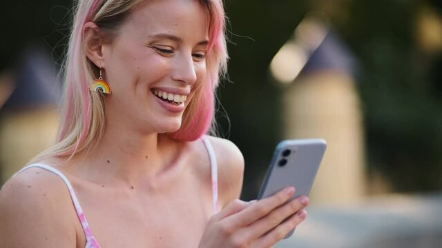 A laughing woman with rainbow earrings is using her phone during pride gay parade