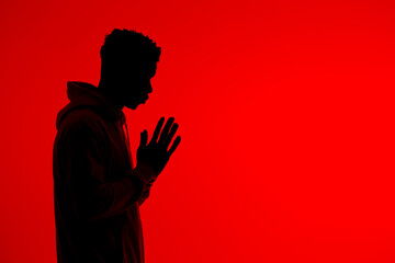 Anonymous black man praying with clasped hands on red background