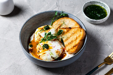 Cilbir or Turkish Eggs. poached eggs topped over herbed greek yogurt, drizzled with hot spiced paprika olive oil. Turkish breakfast in a grey bowl on marble background. shakshuka with pepper.