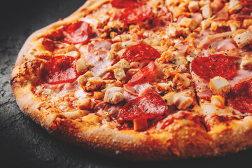 Pizza with Mozzarella cheese, salami, chicken meat, bacon, ham, Tomato sauce, pepper, spices. Italian pizza on Dark grey black slate background