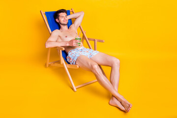 Photo of attractive pretty young guy shirtless having rest deck chair drinking beverage isolated...