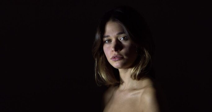 A slo-mo of a naked sexy Caucasian woman looking at the camera and blinking on a black background