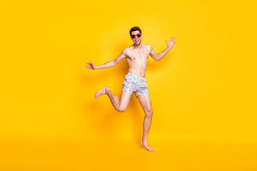 Fototapeta na wymiar Photo of pretty impressed young guy shirtless wear dark glasses smiling dancing isolated yellow color background