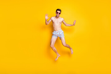 Fototapeta na wymiar Full length photo of funny brunet young guy jump wear shorts eyewear isolated on yellow color background