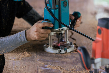 Selective focus. Closeup hand of carpenter use electric trimmer carved on the wooden. Craftsman...