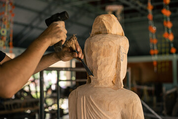 Selective focus. Asia craftsman professional carving buddha statue with chisel in workshop. Artist...