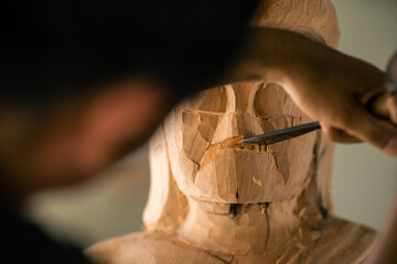 Selective focus. Asia craftsman professional carving face buddha statue with chisel in workshop....