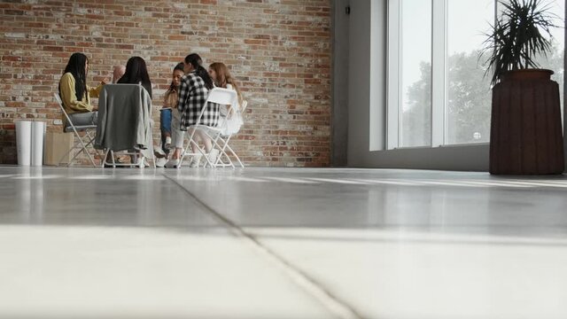 Side view of a multinational businesswomen sitting on the chairs in a circle and discussing work projects in office