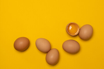 Organic brown chicken eggs and one broken egg with yolk on yellow background. Happy Easter. Patterns.