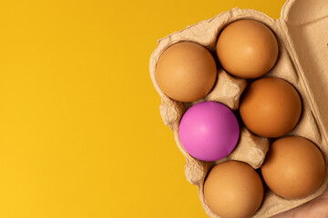 Easter brown chicken eggs in eco basket and one pink egg on yellow background. Fresh egg on morning breakfast, flat lay, copy space.