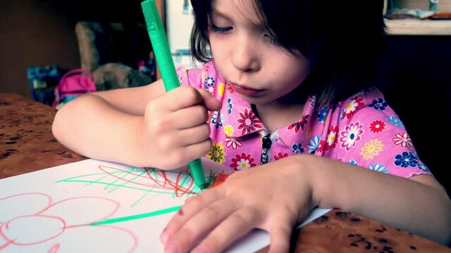 little girl of three years old draws with colored pencils on paper. Wrong fist holding pencil. Paints a flower.