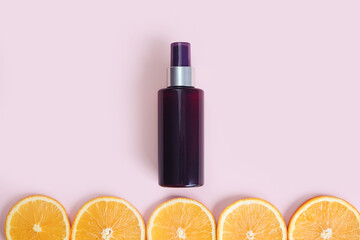 Unbranded dark brown spray bottle and line of orange slice circles on pink background. Cosmetic packaging mockup. Template, front view. Natural organic spa Body mist. Cream bottle with vitamin c.