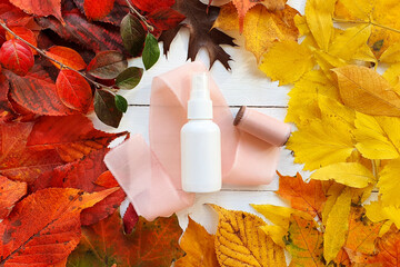 Unbranded white cosmetic spray bottle, silk pink ribbon and round frame of bright autumn or fall...