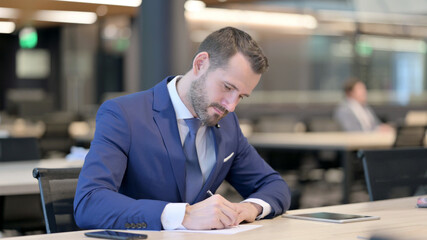 Pensive Middle Aged Businessman Writing on Paper, Thinking