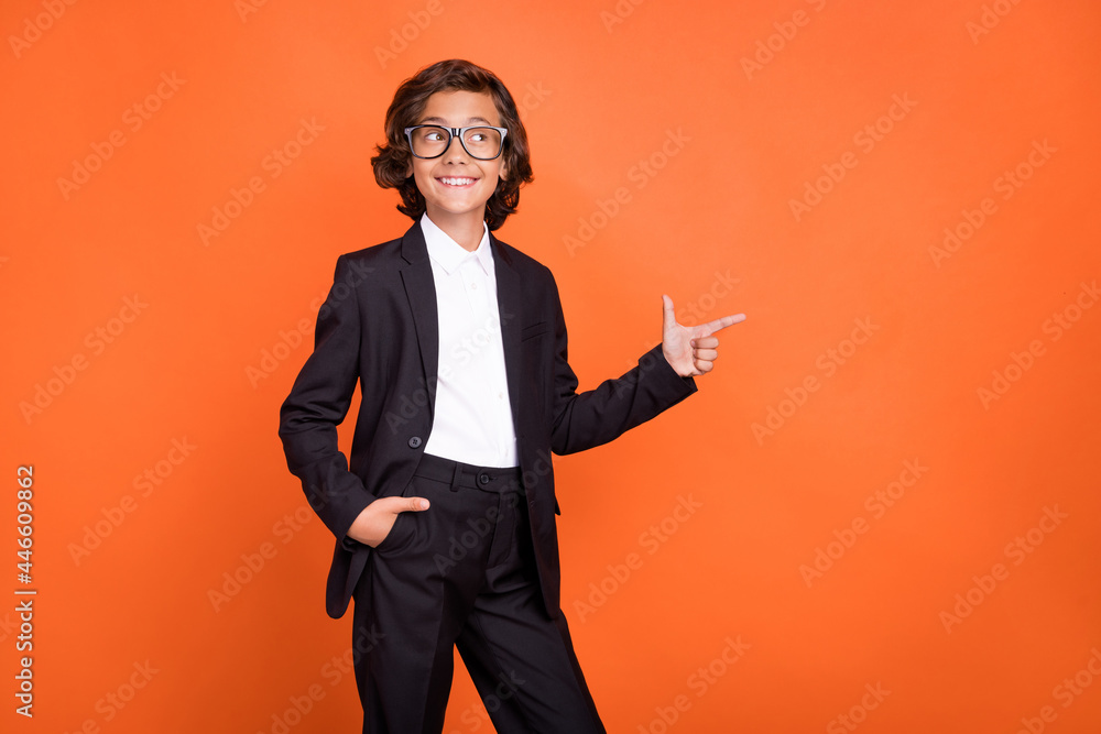 Sticker Photo of young happy amazed positive boy look point index finger empty space isolated on orange color background