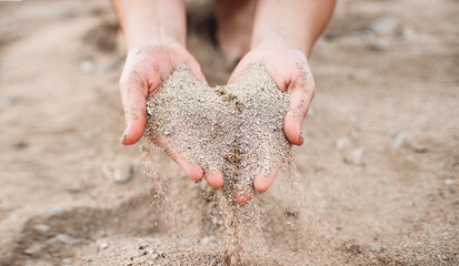 A person puts coarse-grained sand in a pile with his hands. beautiful sand in women's hands crumbles