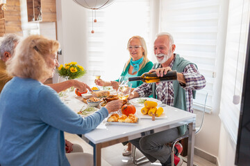 Senior friends pouring wine while having Thanksgiving dinner