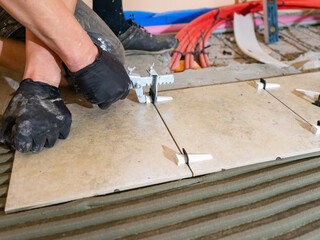 Workers are using plastic clamps and wedges to leveling the ceramic tile on the floor. Tile leveling system.