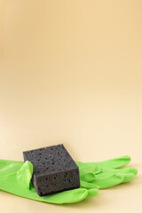 Black dishwashing sponge and green rubber gloves on neutral beige background, cleaning concept