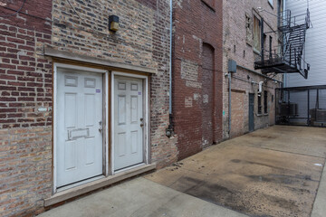 Two dirty white doors on the back of a vintage brick building with steel fire escape