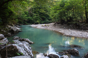 blue mountain river flowing among big stones in greenforest in caucasus