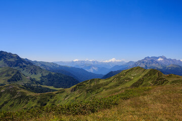 landscape of blue sky and green grass of alpine meadows with rocky mountains valley far away