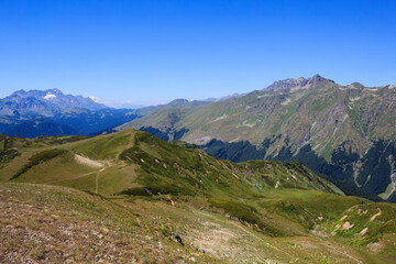 landscape with footpath in alpine meadows and high rocky mountains covered with snow