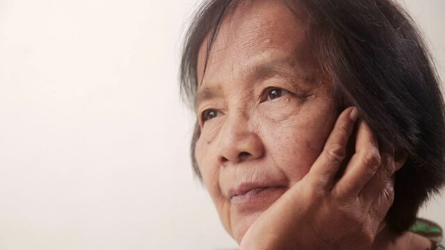 Close-up of an Asian elderly woman's face Sitting with hands on cheeks, feeling stressed, worried, afraid of getting sick. Elderly people have short-sightedness problems, blurry vision.