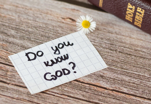 Do you know God and Jesus Christ? Closeup of a handwritten note on wooden background with holy Bible book and small flower. Christian biblical concept of faith, hope, love, relationship with the LORD.