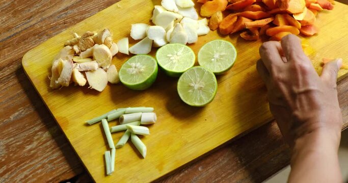 Close up of woman cutting herbs, roots and spices for homemade Jamu drink- Indonesian herbal beverage with natural ingredients: turmeric, ginger, lime, lemongrass, tamarind, lemon in kitchen.