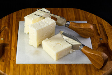 Feta cheese on marble and wooden cheese cutting board with fork and knife