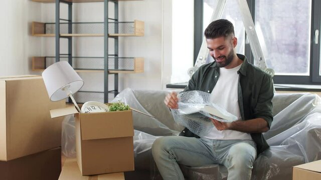 moving, people and real estate concept - happy smiling man with boxes unpacking things at new home