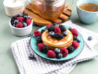 Stack of pancakes with raspberries and blueberries served with green tea