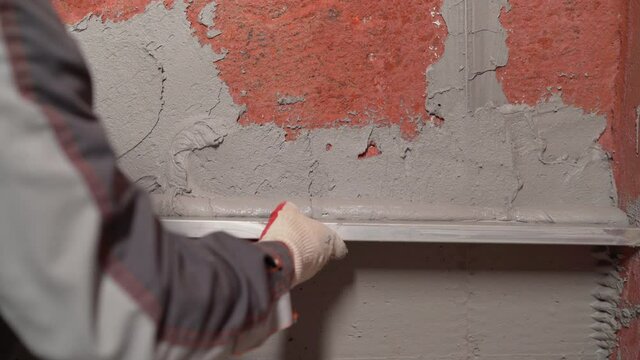 Plasterer using screeder smoothing putty plaster mortar on wall. Smoothing out putty on the wall.