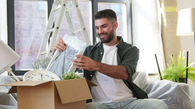 moving, people and real estate concept - happy smiling man with boxes unpacking things at new home