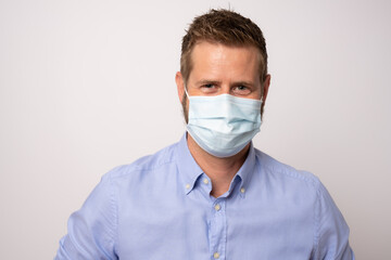 Portrait of handsome young businessman with surgical medical mask looking at camera.