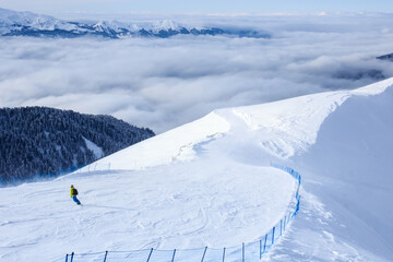 snowboarder on his descent on the trail in mountain ski resort and forest clouds behind