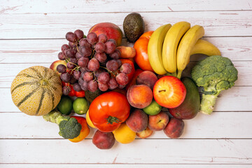 Top view image of seasonal fruits and vegetables with red tomatoes, red grapes, melon and watermelons, red and yellow peaches, broccoli and limes on white wooden background.