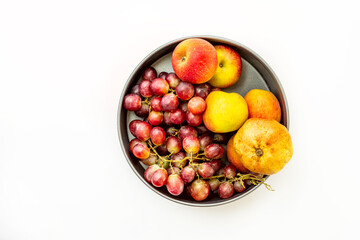 Fruit bowl seen from the top with bunches of red grapes, apples and a pomegranate on white background