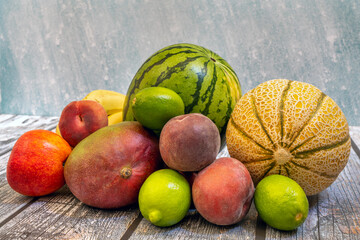 Ripe fruits ready to eat on a summer day. Red peaches, green limes, melons and watermelons, African mangoes on wooden table