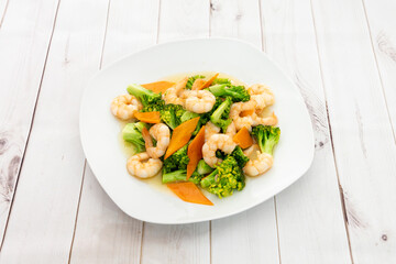 Plate of cooked peeled prawns with broccoli al dente and carrot slices on white plate