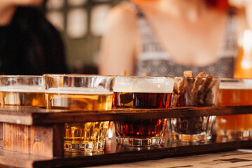 Set of different types of beer with snack croutons on a wooden stand in a dark bar close-up