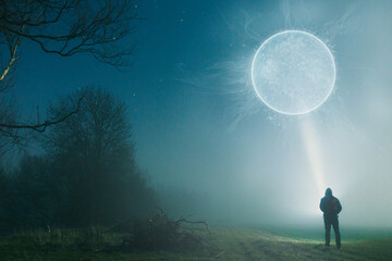 Fototapeta na wymiar A man standing with a torch looking up at a glowing science fiction portal. On a foggy, winters night in the countryside.